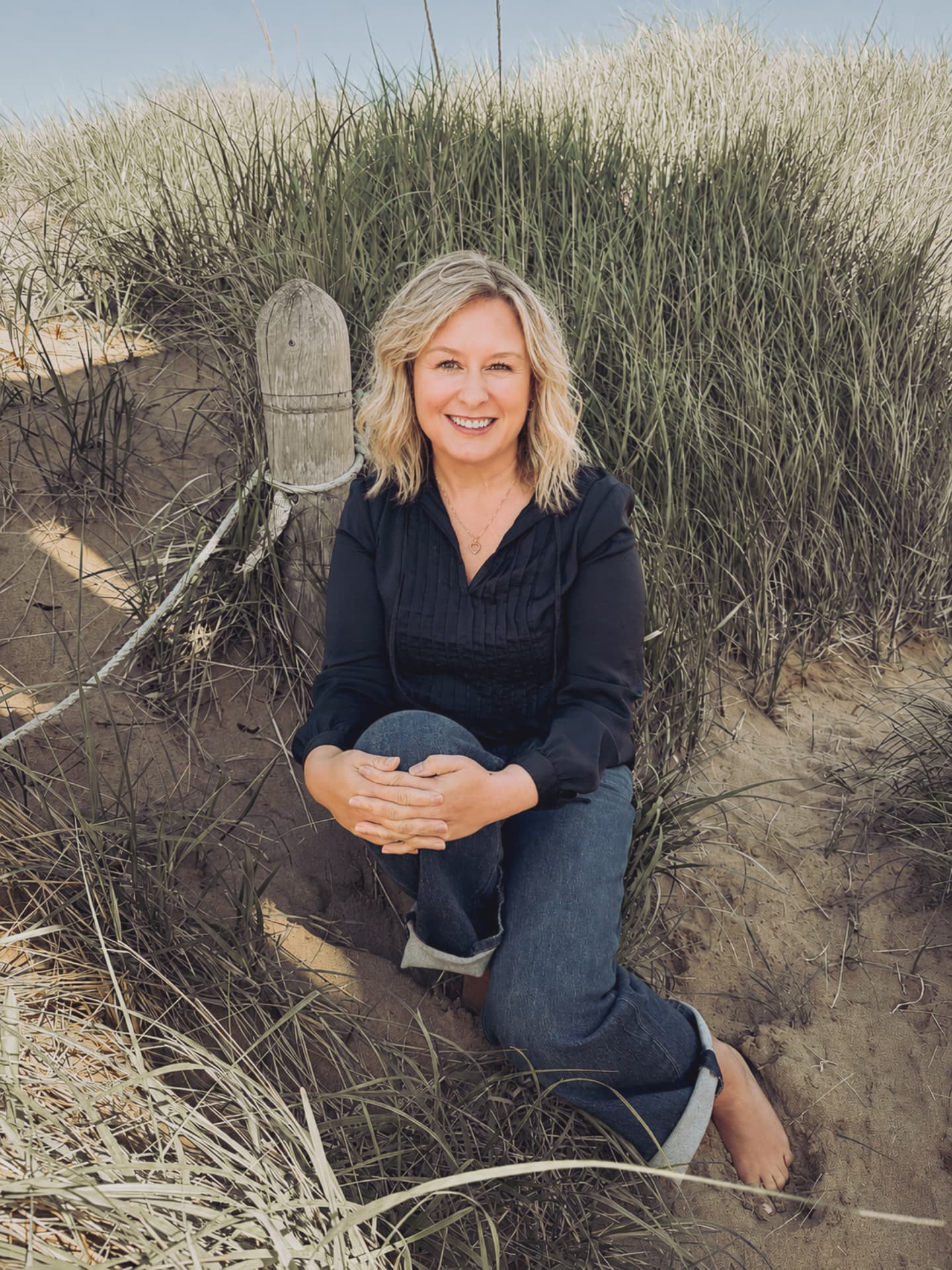 Trish, founder of Fare-Well Co., sitting in the dune grass on a Prince Edward Island beach